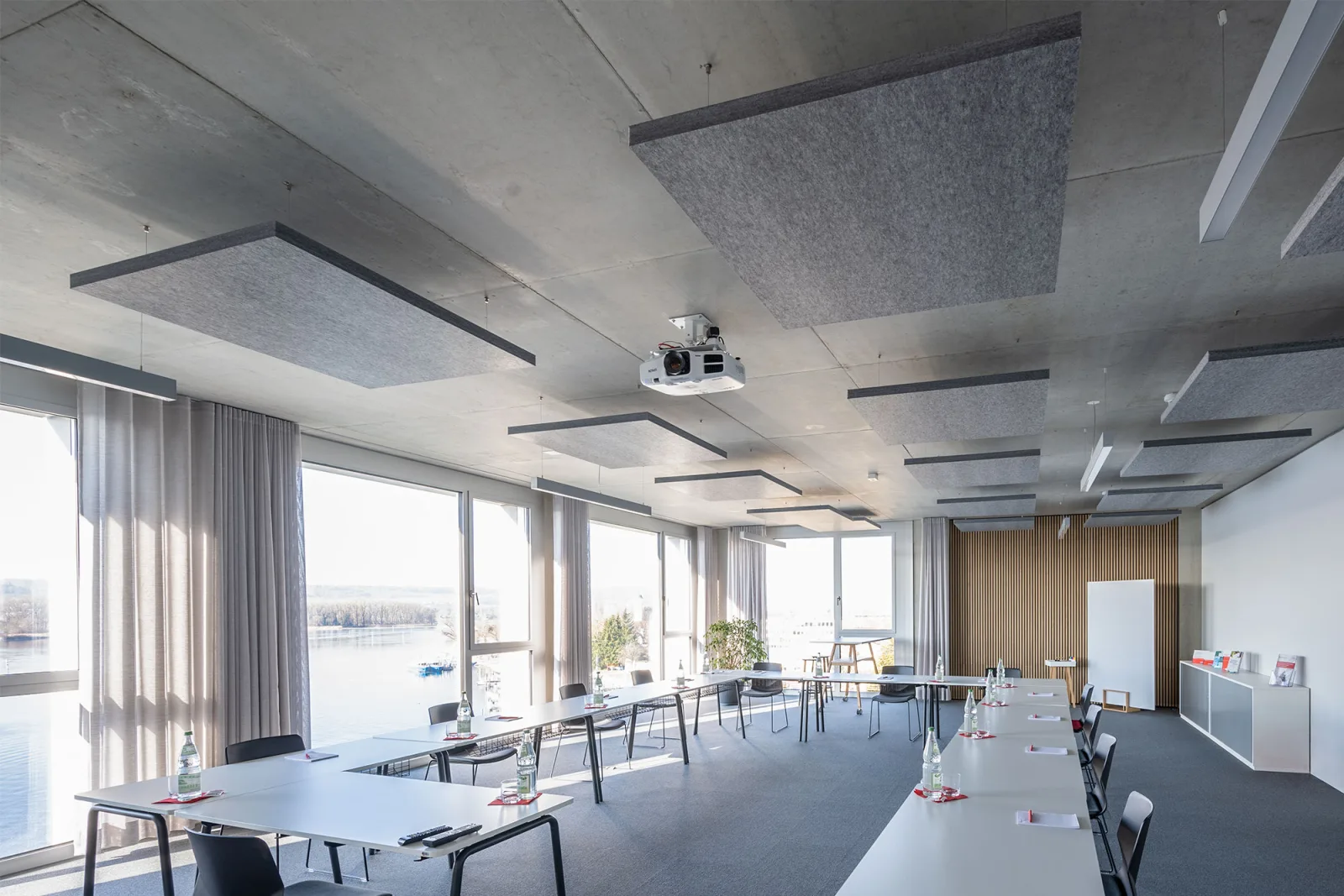Seminarraum mit frei abgehängten grauen Deckensegeln, Beamer an der Decke und Tischen in U-Form