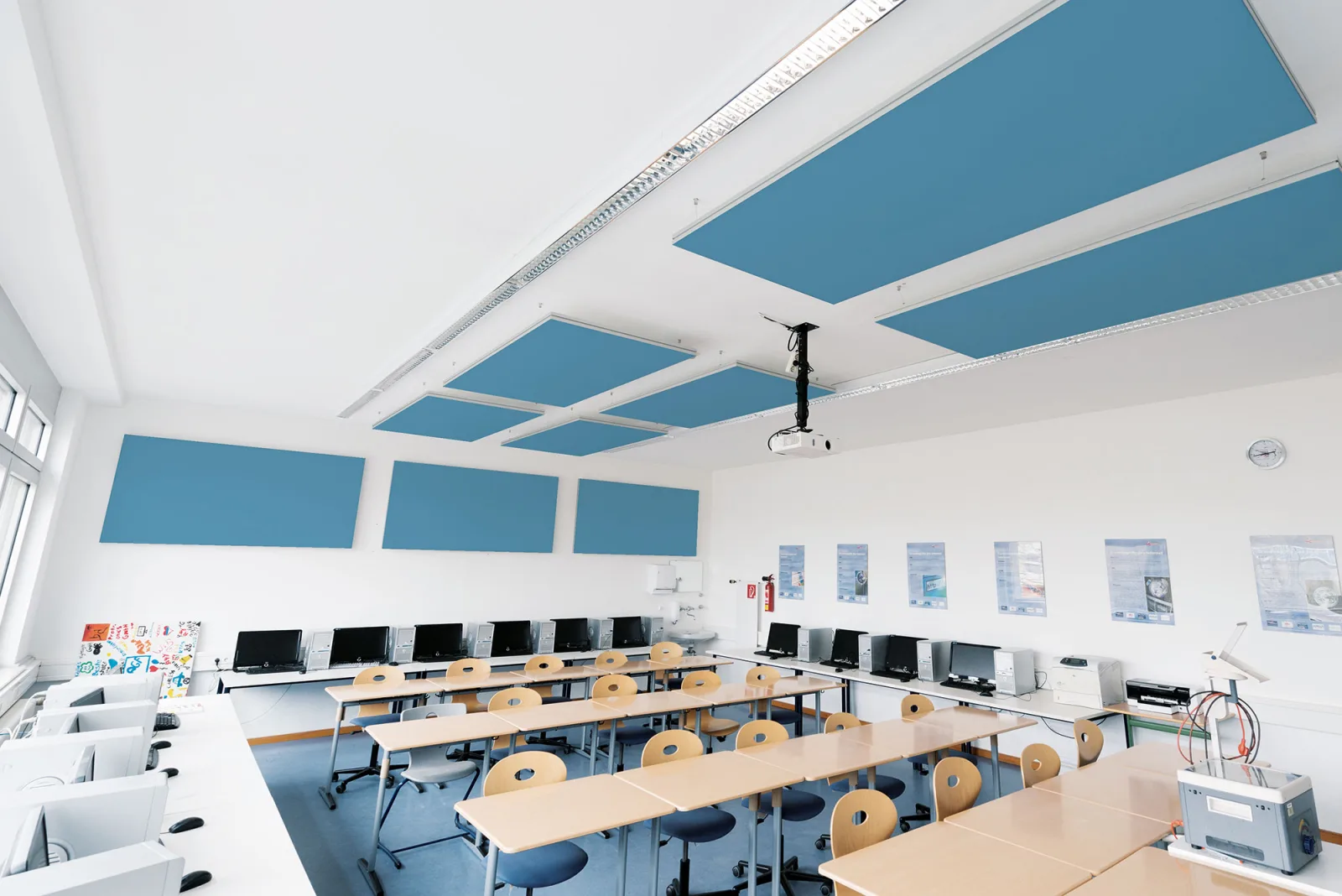 Klassenraum mit blauen Deckensegeln und drei blauen Wandabsorbern, davor Tischreihen und eine Reihe Computerarbeitsplätze