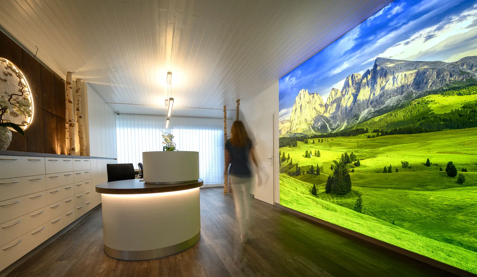 Praxisempfang mit runder Theke und großer hinterleuchteter Bildwand mit Bergmotiv an der Wand gegenüber