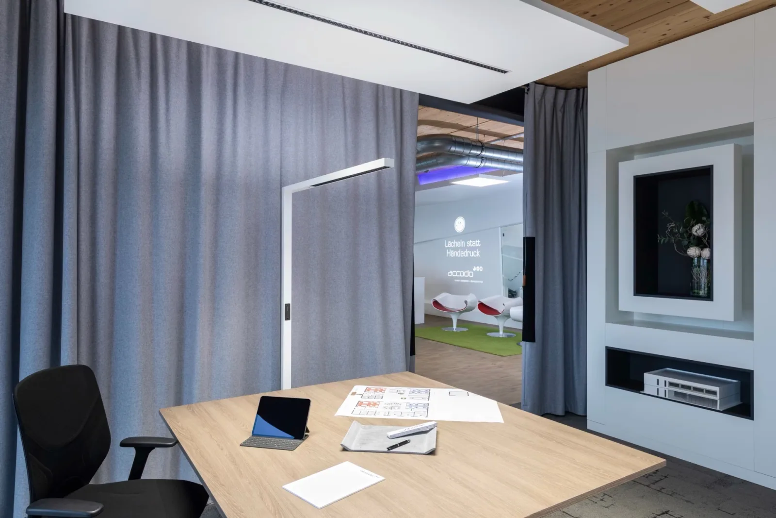 Weiße Stehleuchte von Accodo über einem Besprechungstisch mit Plänen und Tablet, dahinter graue Vorhänge und eine Ausstellungsfläche