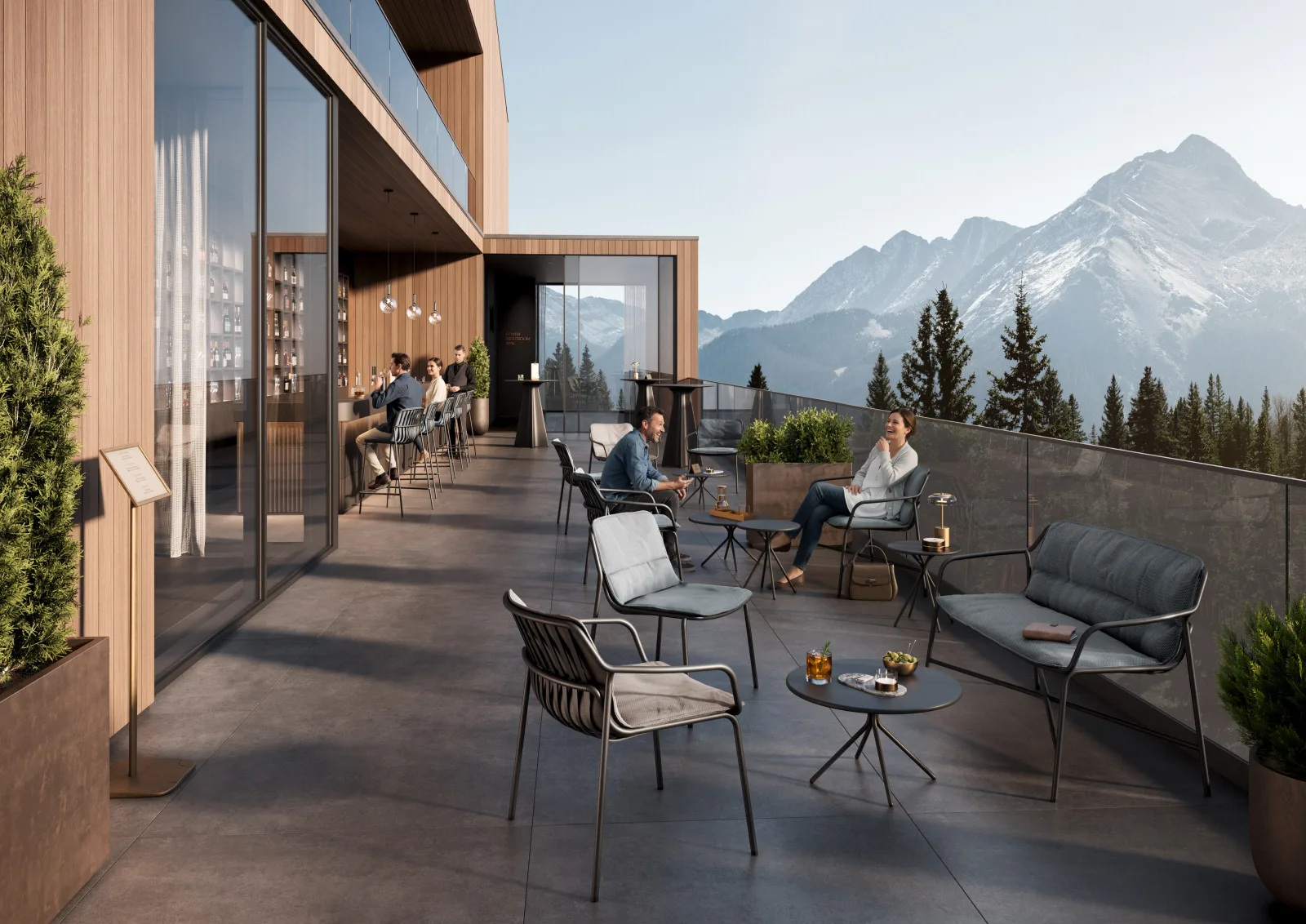 Dachterrasse eines Hotels mit Loungesesseln, Zweisitzer und kleinen Tischen, dahinter eine Bar hinter Glas und Bergpanorama