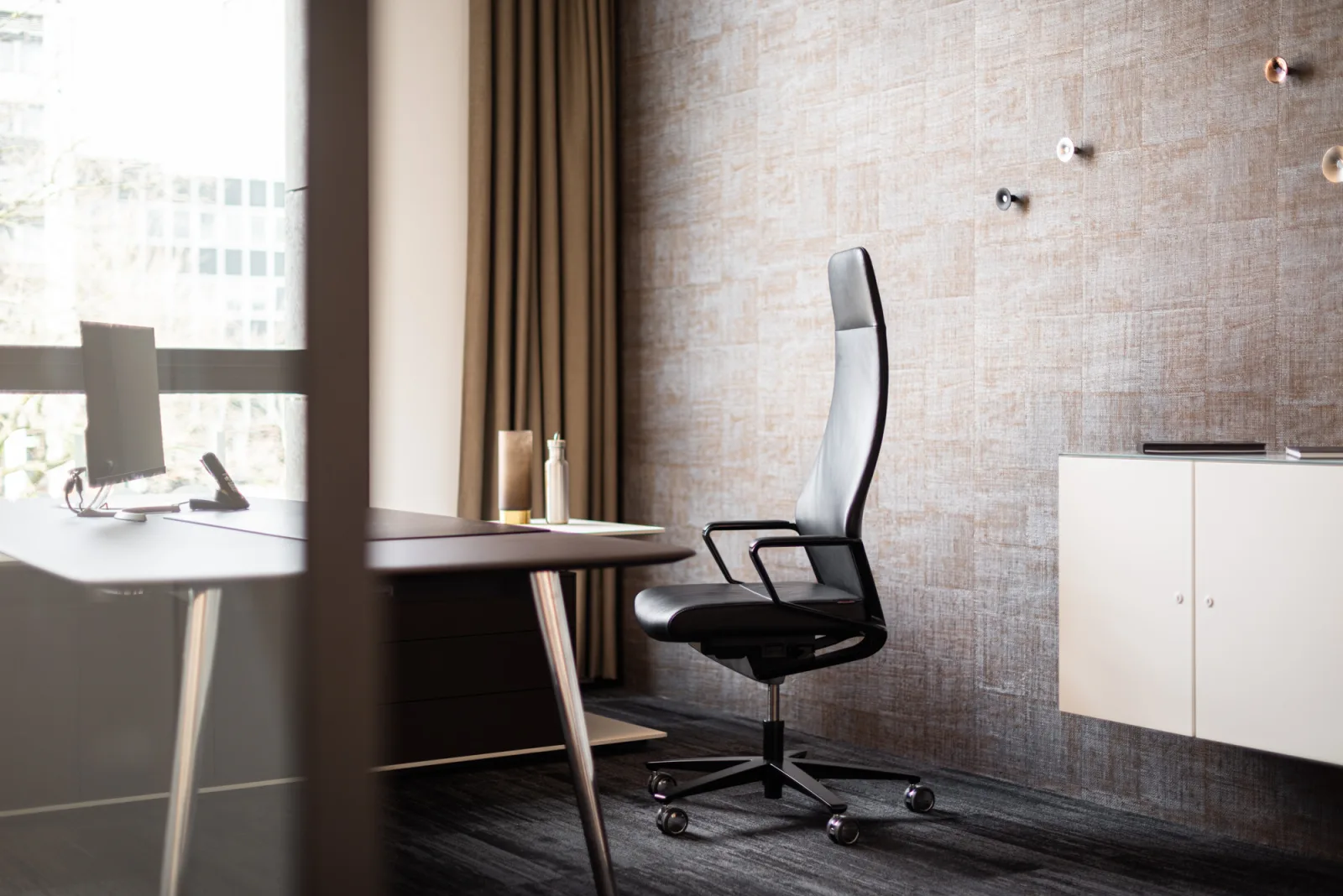 Einzelbüro mit Schreibtisch, hohem Lederdrehstuhl und Sideboard vor einer Ziegelwand