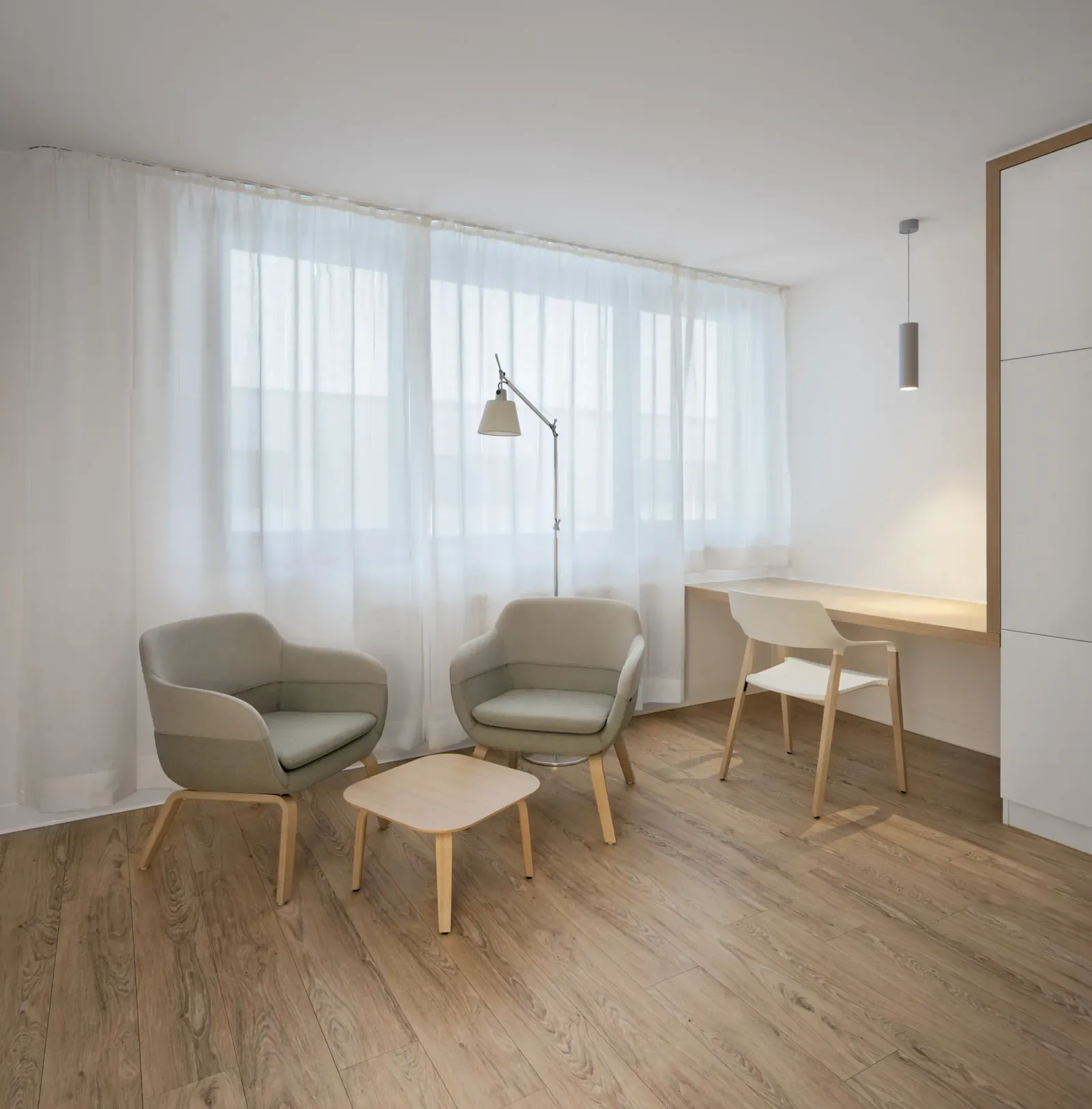 Heller Raum mit Schreibtisch am Fenster, zwei Polstersesseln und einem Vorhang als Raumteiler