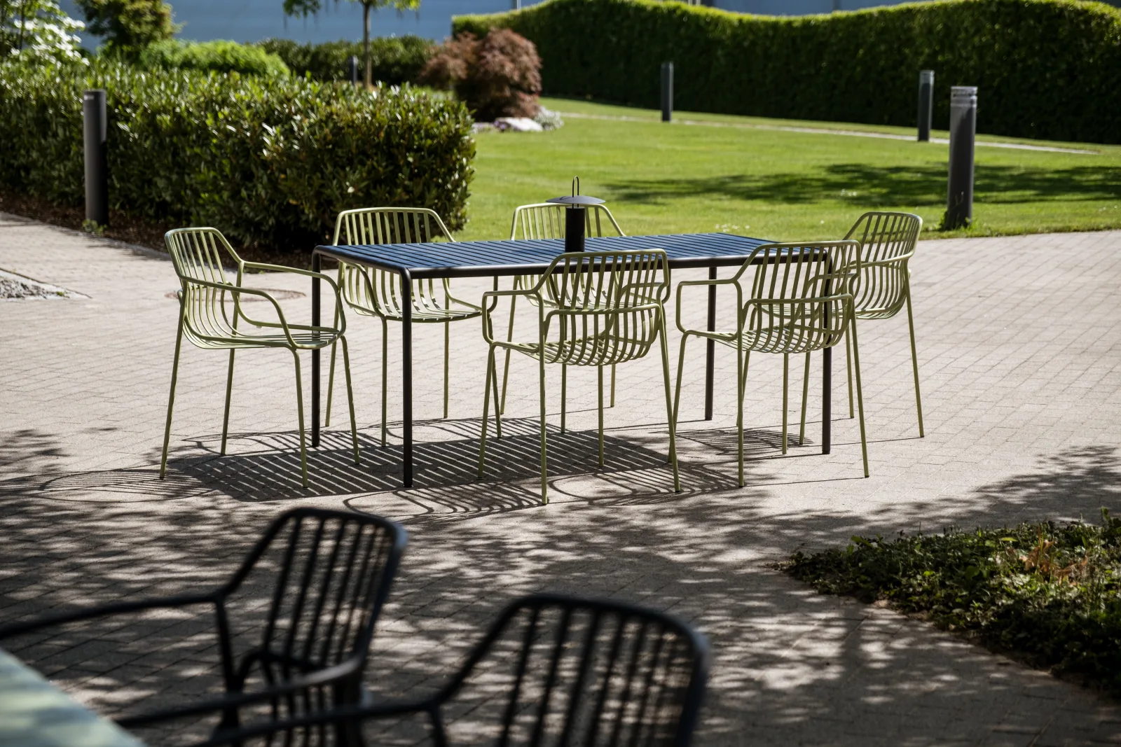 Gartenterrasse mit Sechser-Tischgruppe, olivgrünen Drahtstühlen und dunkler Tischplatte