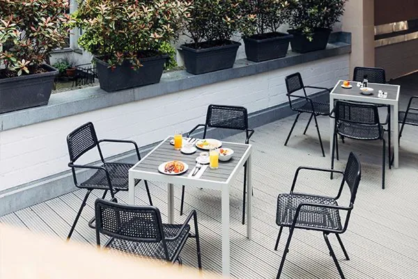 Terrasse von oben mit zwei weißen Tischen, schwarzen Netzgeflecht-Stühlen und aufgedecktem Frühstück