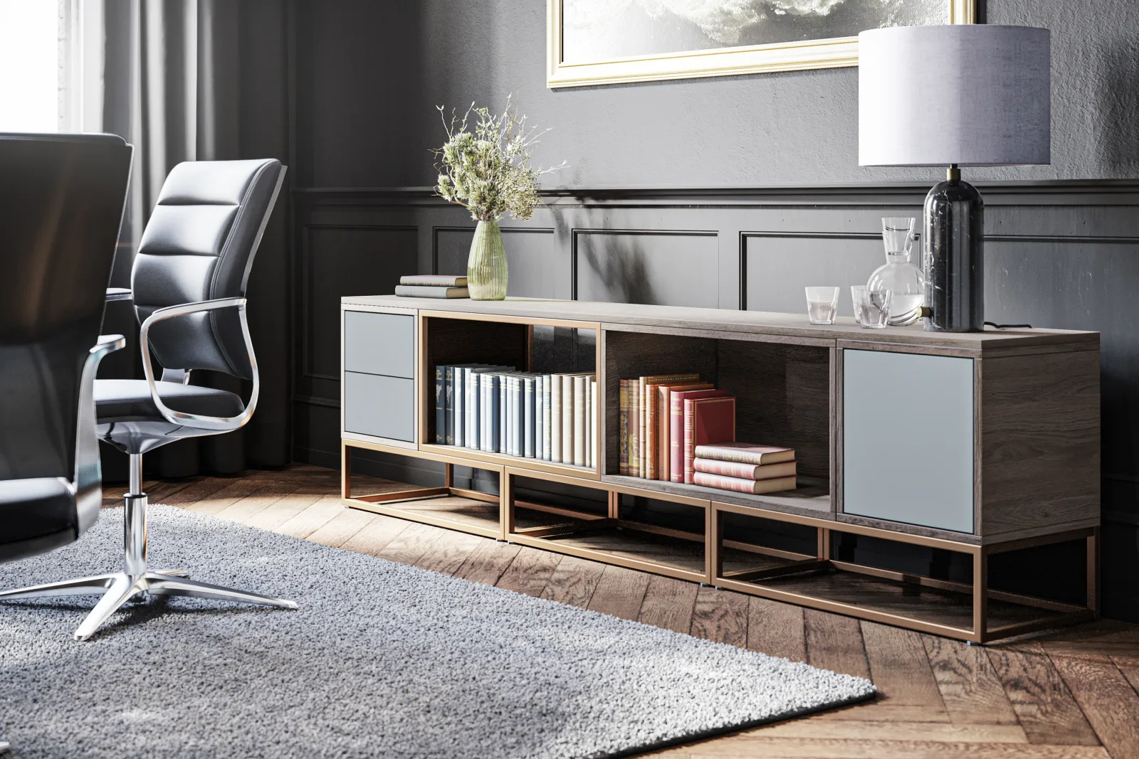 Niedriges Sideboard aus Holz mit hellgrauen Fronten und Messinggestell vor dunkel vertäfelter Wand, davor ein schwarzer Lederdrehstuhl