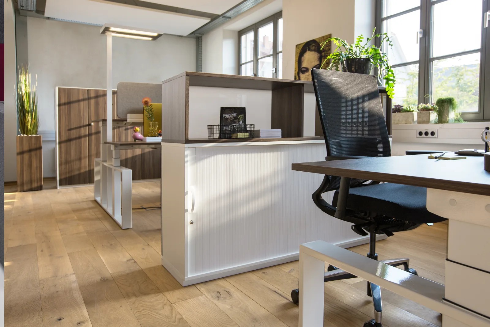 Weißes offenes Regal als Raumteiler neben einem Rollladenschrank in einem Büro mit Holzboden