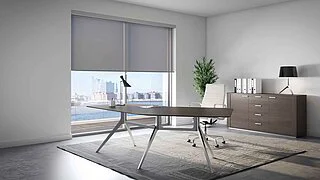 Arbeitszimmer mit Schreibtisch und Sideboard, vor der Fensterfront ein graues Rollo bis zur halben Höhe