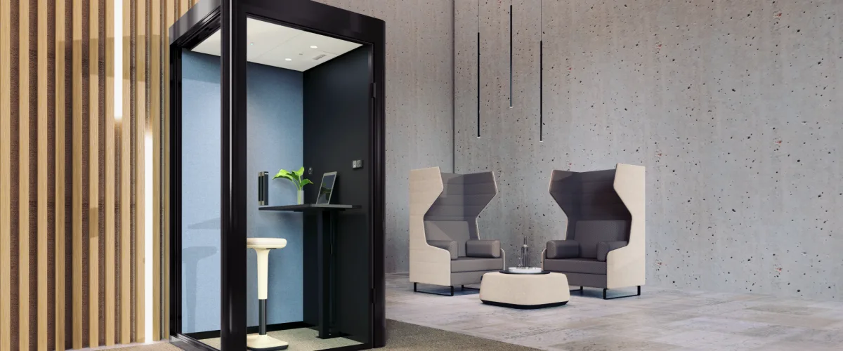 Schwarze Telefonbox cube 4.0 telephone von Bosse in einem Bürofoyer, Glastür geöffnet, innen ein Stehtisch mit Laptop und ein Stehhocker, daneben zwei Sessel mit hoher Rückenlehne