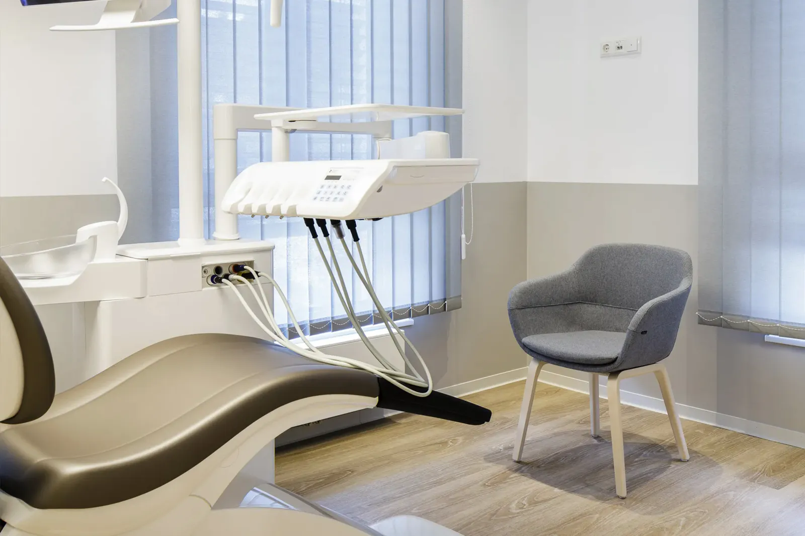 Behandlungszimmer mit Behandlungseinheit, Speifontäne und einem gepolsterten Besucherstuhl am Fenster